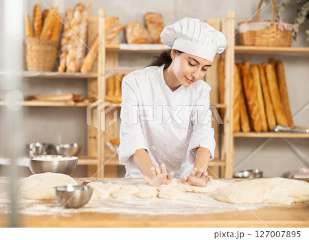 Young female baker kneading dough on table Young female baker kneading dough on table 127007895
