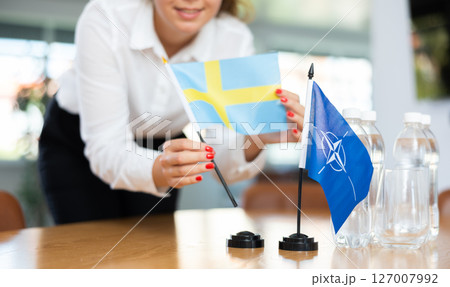 Employee of delegation prepares negotiating table - sets up flag of NATO (OTAN) and Sweden Employee of delegation prepares negotiating table - sets up flag of NATO (OTAN) and Sweden 127007992
