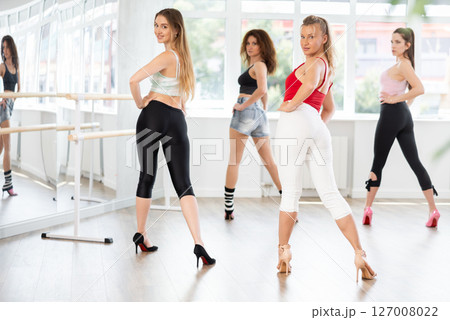 During lesson, girl learn to move and perform dance in heels with women companions, back view 127008022