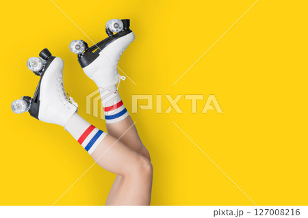 Playful roller skating with white boots and stripe socks on bright yellow background Playful roller skating with white boots and stripe socks on bright yellow background 127008216
