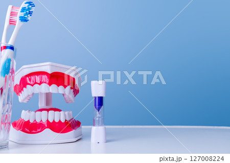 Dental hygiene tools with toothbrush, model dentures, and timer on blue background 127008224