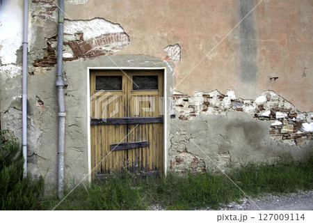 Old wooden door on a house wall. Conceptual image. Wooden Door on an Old House Wall. Architectural Details Worn and Weathered by Time.  127009114