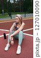The concept of energy, vitality, well-being. A toned, beautiful blonde in sports clothes is relaxing after a workout outdoors. She's sitting on a sports basketball court 127010090