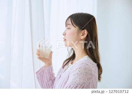 窓際でグラスに入ったジュースを飲む女性 127010712