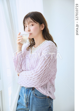 窓際でグラスに入ったジュースを飲む女性 127010719