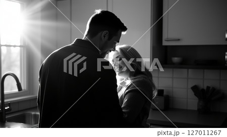 Married couple hugging in the morning in the kitchen. Man and woman in love hugging in the rays of the morning sun. Monochrome image. Married couple hugging in the morning in the kitchen. Man and woman in love hugging in the rays of the morning sun. Monochrome image. 127011267