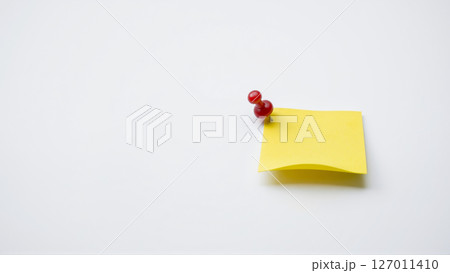 A yellow sheet of paper for notes is attached with a red pushpin to a white wall 127011410