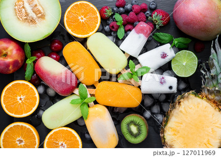 In the center on ice cubes variety of sorbet and ice cream cones near ingredients fruits and berries on black background. Summer coolness of ice cream and sorbet cones. Horizontal. Top view. In the center on ice cubes variety of sorbet and ice cream cones near ingredients fruits and berries on black background. Summer coolness of ice cream and sorbet cones. Horizontal. Top view. 127011969