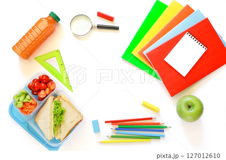 School supplies, lunch box with sandwiches, pieces of cucumbers and carrots, cherries, apple, bottle of juice on white background, back to school concept with copyspace. Horizontal. Top view. 127012610