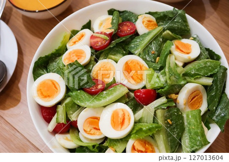 close up of homemade salad of boiled egg cut in slices, cherry tomato, lettuce in a big white bowl  with pumpkin cream soup in the side 127013604