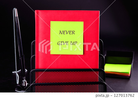 Business development challenge concept and effort success idea. Never give up written on a green sticker on a red business book on a black background 127013762