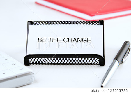Words BE THE CHANGE on a white business card, front view 127013783