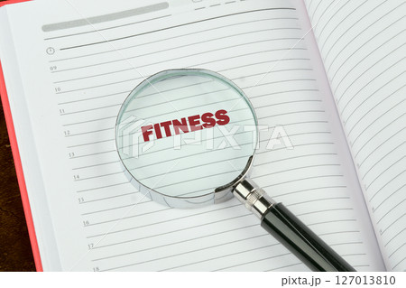 Business and Invest in your Health concept. Concept words FITNESS focused through a magnifying glass in a notebook 127013810