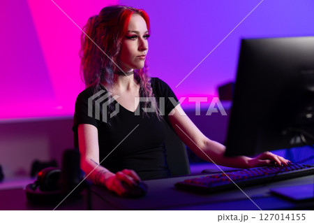 Focused female gamer interacting with computer in vibrant neon-lit gaming space 127014155