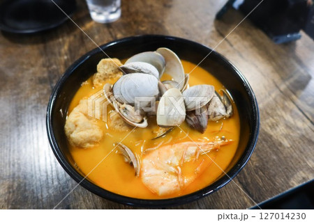 close up of laksa rice noodles with seafood including shells, prawn, clam, tofu puff in a black bowl 127014230