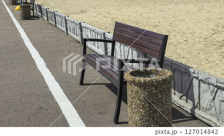 Wooden benches and trash bins line the side of the road in a park recreation area Wooden benches and trash bins line the side of the road in a park recreation area 127014842