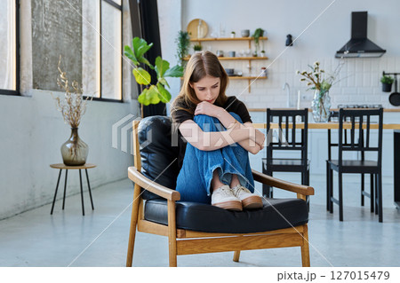 Sad stressed young woman sitting at home on armchair Sad stressed young woman sitting at home on armchair 127015479