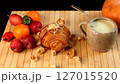 Croissant near ceramic mug filled with creamy vegetable beverage, fruits scattered on bamboo mat, vibrant autumn harvest scene highlighting fresh seasonal produce, rustic textures, natural light. 127015520