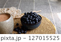 Rustic ceramic cup containing creamy smoothie paired with dark blue bowl of vibrant blueberries on beige woven surface reflects eco-friendly, nutrient-rich clean eating lifestyle. 127015525