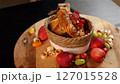 Pastry with roasted tomatoes in woven basket, surrounded by red apples, green grapes, yellow and orange tomatoes, arranged on wooden board emphasizing rustic tones and natural materials. 127015528
