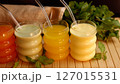 Juices in green, yellow, and cream shades with straws on rustic wooden board surrounded by fresh mint. Vibrant setup suggests healthy, refreshing drinks for clean, eco-conscious lifestyle. 127015531