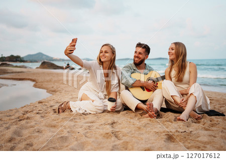 Group of Friends Relaxing on the Beach with Guitar on a Sunny Day 127017612