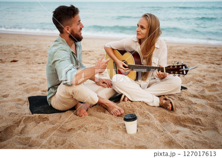 Romantic Couple Smiling on Beach While Girl Plays Guitar at Sunrise 127017613