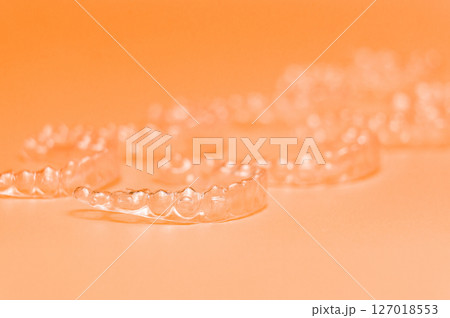 Orthodontic silicone aligner background. Advertisement of invisible braces retainer. Medical website concept. Pros and cons of aligners. peach saturated background Orthodontic silicone aligner background. Advertisement of invisible braces retainer. Medical website concept. Pros and cons of aligners. peach saturated background 127018553