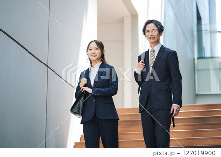 オフィスビルの階段を歩くスーツを着た若い男女 127019900