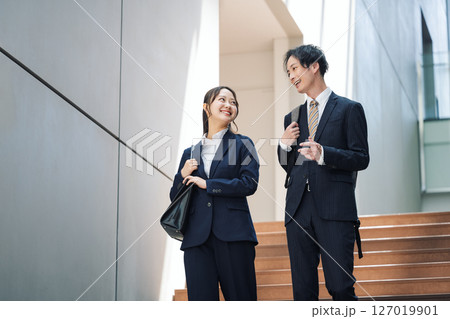 オフィスビルの階段を歩くスーツを着た若い男女 オフィスビルの階段を歩くスーツを着た若い男女 127019901