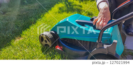 An elderly woman takes care of garden equipment - a lawn mower, wipes it. The concept of housework, gardening, gardening. 127021994