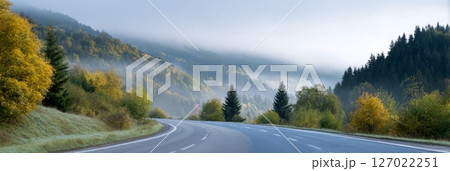 A winding road meanders through a misty forest filled with stunning fall foliage at dawn 127022251
