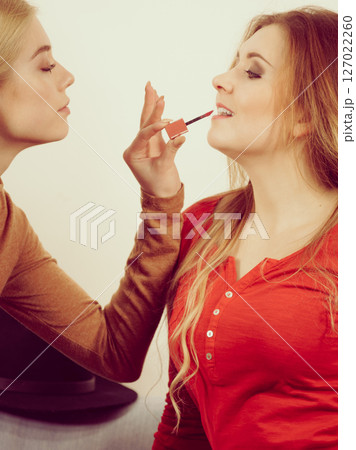Woman applying her friend lipstick on lips Woman applying her friend lipstick on lips 127022260