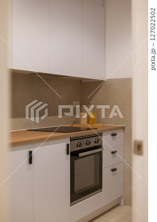 Minimalist kitchen with white cabinets, wood countertop, electric stove and jars of pasta and grains 127022502