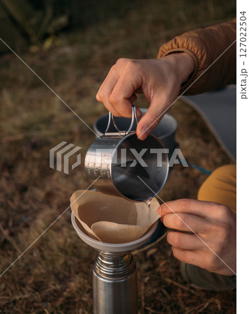Close view of outdoor coffee brewing with metal cup pouring into paper filter funnel 127022504