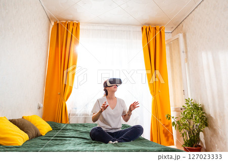 Female tech enthusiast enjoying immersive VR simulation while at home, interacting with smart technology. Low angle view. Wide shot Female tech enthusiast enjoying immersive VR simulation while at home, interacting with smart technology. Low angle view. Wide shot 127023333