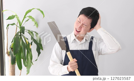 ノコギリを持つ悩む表情のエプロン姿の男性 127023587