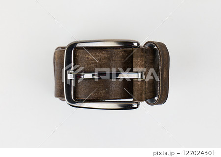 A brown leather belt with a shiny silver buckle placed on a white background. High quality photo 127024301