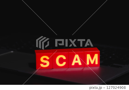 Red Scam Blocks Highlighting Cyber Fraud. Spelling SCAM placed on laptop keyboard in dark environment, symbolizing cyber fraud, phishing, scammer, cybersecurity threats, and online deception risks. 127024908