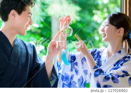 浴衣姿の男女が風鈴を指さしながら笑顔を交わす夏のひととき 127026902