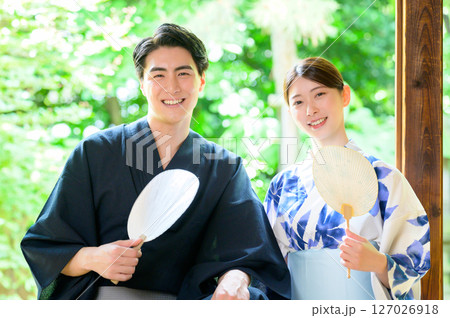 緑の背景を前に団扇を手に笑顔を見せる浴衣姿の男女 127026918