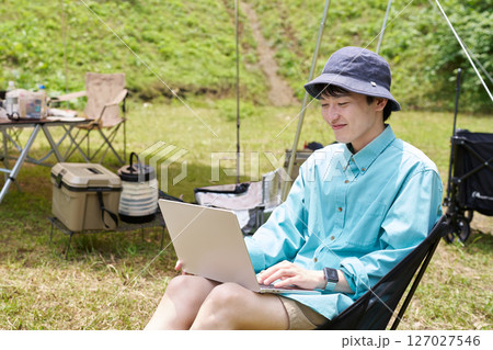 キャンプ場でノートPCを使う若い男性 127027546
