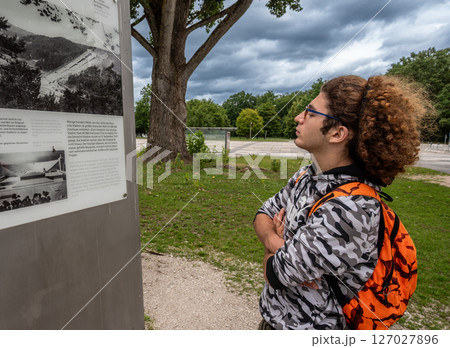 Nuremberg, Germany, August 3, 2023. A young Caucasian man with curly hair and glasses looks at information signs at the Nazi party rally site. Nuremberg, Germany, August 3, 2023. A young Caucasian man with curly hair and glasses looks at information signs at the Nazi party rally site. 127027896