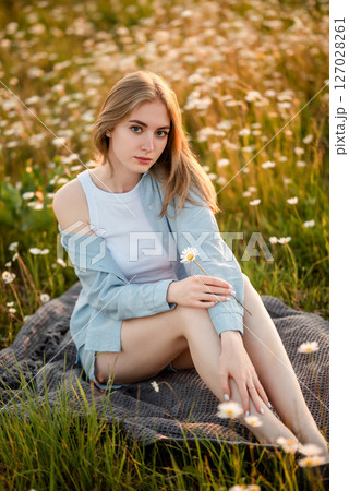 Young Woman Relaxing in a Daisy Field Holding a Flower 127028261