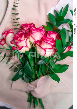 A bouquet of roses is wrapped in a coarse knit woolen sweater. 127028760