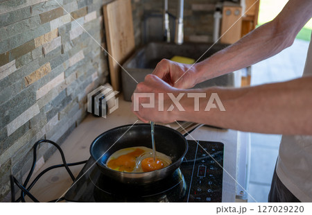 Person cooking scrambled eggs in a frying pan on an induction cooktop, concept of home cooking Person cooking scrambled eggs in a frying pan on an induction cooktop, concept of home cooking 127029220