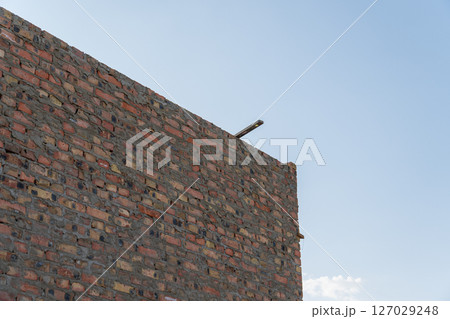 A sturdy brick wall stands tall under a clear blue sky, showcasing the progress of construction in an urban setting 127029248