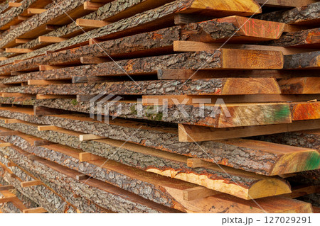 Piles of hardwood planks are arranged neatly at a lumber yard, showcasing natural textures, colors, and light reflecting off the surfaces 127029291