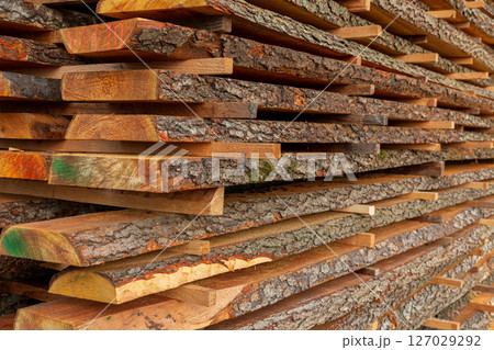 A collection of neatly stacked wooden planks reveals rich textures and colors, illustrating woodworking materials at a lumber yard 127029292
