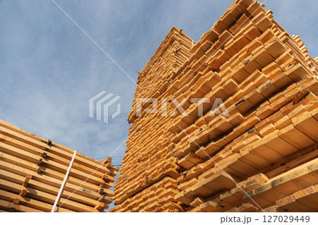 Tall stacks of wooden planks are neatly arranged at a lumber yard, showcasing a variety of timber types against a bright sky Tall stacks of wooden planks are neatly arranged at a lumber yard, showcasing a variety of timber types against a bright sky 127029449